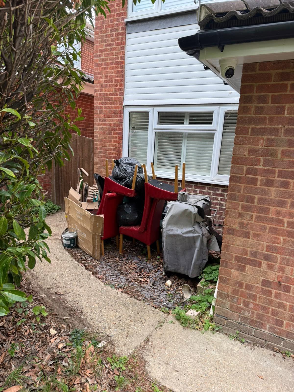 A side passage stacked with old chairs, bin bags and rubbish before clearance